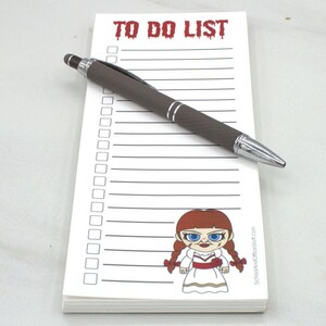 May include: A white notepad with the words "TO DO LIST" in red, a cartoon image, and a brown pen with silver accents. The notepad has a lined layout with check boxes.