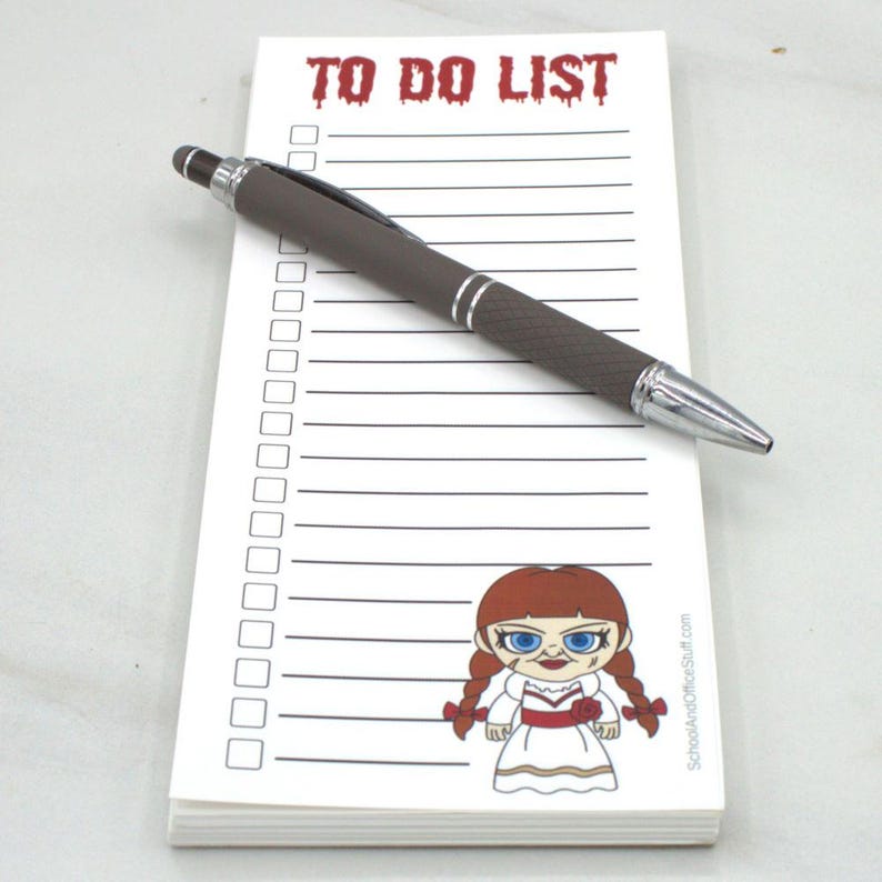 May include: A white notepad with the words "TO DO LIST" in red, a cartoon image, and a brown pen with silver accents. The notepad has a lined layout with check boxes.