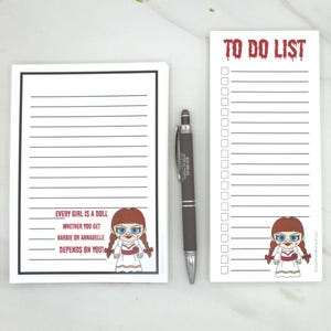 May include: Two white notepads with black lines and text. One notepad says "EVERY GIRL IS A DOLL WHETHER YOU GET BARBIE OR ANNABELLE DEPENDS ON YOU!" with a doll graphic. The other says "TO DO LIST" with a doll graphic. A pen is between the notepads.