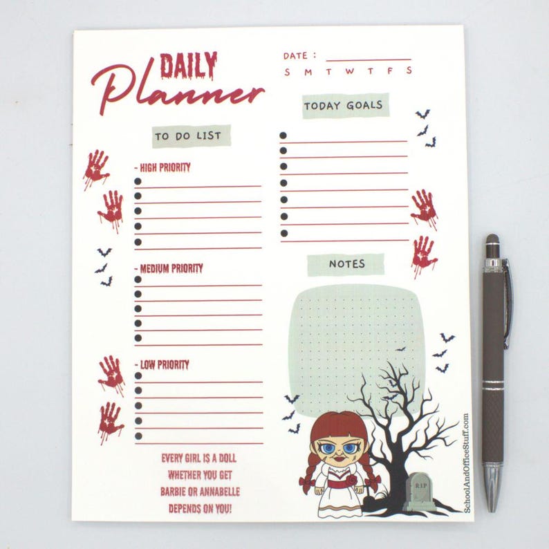 May include: A white daily planner with a spooky theme. The planner features sections for to-do lists, notes, and today's goals. Red handprints and bats decorate the page. A brown pen rests beside the planner. The text reads "Daily Planner".