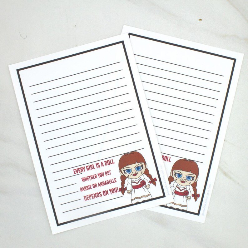 May include: Two white lined notepads with black borders. Each notepad features a cartoon doll illustration and the text: "EVERY GIRL IS A DOLL WHETHER YOU GET BARBIE OR ANNABELLE DEPENDS ON YOU!"