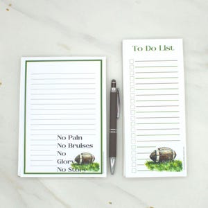 May include: A set of two white notepads with green borders and a pen. One notepad has lines and the text "No Pain No Bruises No Glory No Story" with a football graphic. The other notepad is a "To Do List" with a football graphic.