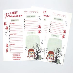 May include: Two white Daily Planner sheets with red accents. Each sheet has a to-do list, today goals, and notes section. The sheets feature a doll graphic, a tree, and the text "EVERY GIRL IS A DOLL WHETHER YOU GET BARBIE OR ANNABELLE DEPENDS ON YOU!"