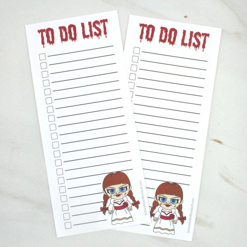 May include: Two white "To Do List" notepads with a red, dripping font. Each notepad has a lined section for writing and a cartoon image of a doll at the bottom. The doll has red hair, blue eyes, and a white dress.
