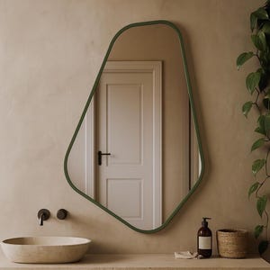 May include: An irregularly shaped mirror with a green frame hangs above a stone countertop. The mirror reflects a white door. A stone sink, black tap, and a woven basket are also visible.