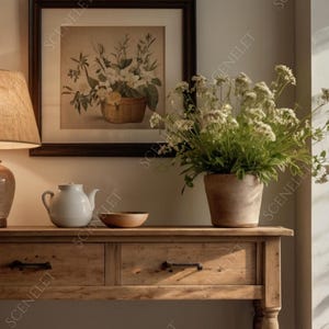 Könnte beinhalten: Rustikale Holzkonsolentisch mit zwei Schubladen, auf dem sich eine Keramiklampe, eine weiße Teekanne und eine kleine Holzschale befinden. Ein gerahmter Blumendruck und eine Topfpflanze ergänzen die Einrichtung.