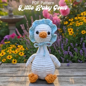 May include: A handmade crochet goose with a white body, orange beak and feet, and a light blue bonnet tied with a bow. The text "Little Baby Goose" is at the top. The goose is sitting on a wooden surface with flowers in the background.