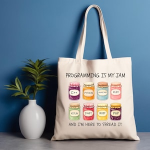 May include: Cream-colored tote bag with the text "PROGRAMMING IS MY JAM" and "AND I'M HERE TO SPREAD IT". The bag features illustrations of jam jars labeled with programming languages such as C++, Python, and Javascript.