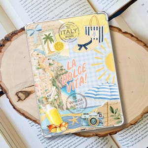 May include: A clear tablet case with a collage design featuring Italian imagery. The design includes a beach scene, a camera, a sun, a hat, and the words "LA DOLCE VITA!" in a colorful, whimsical style.