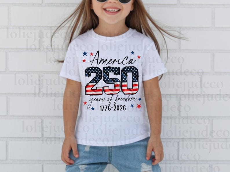 May include: A white short-sleeve t-shirt featuring a graphic with the text America 250 years of freedom 1776-2026. The numbers 250 are filled with a red, white, and blue American flag pattern, surrounded by small red and blue stars.