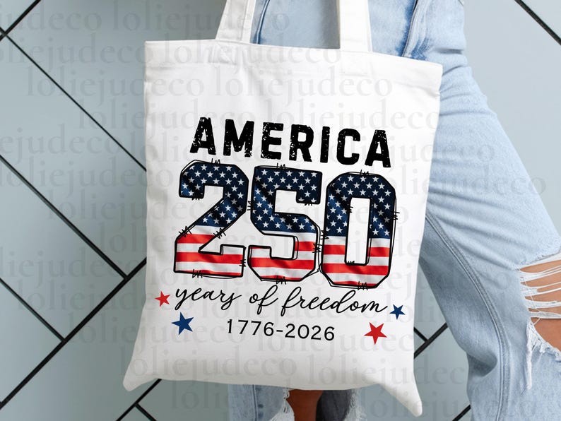 May include: A white canvas tote bag featuring the black text AMERICA above the large number 250, which is filled with a red, white, and blue American flag pattern. Below, the text reads years of freedom 1776-2026 with small red and blue stars.