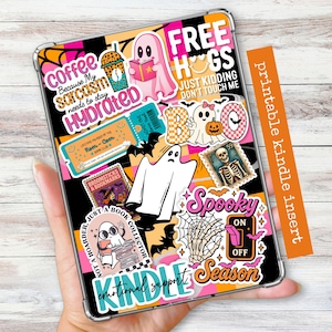 May include: A clear Kindle case decorated with Halloween-themed stickers. The stickers feature ghosts, bats, and phrases like "Spooky Season" and "Free Hugs." An orange strip on the side reads "printable kindle insert."