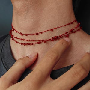 Puede incluir: Un collar rojo de tres hilos con un dise&ntilde;o de goteo. El collar se lleva alrededor del cuello. El collar est&aacute; hecho de un material rojo con un acabado brillante. El collar es una pieza de joyer&iacute;a &uacute;nica.