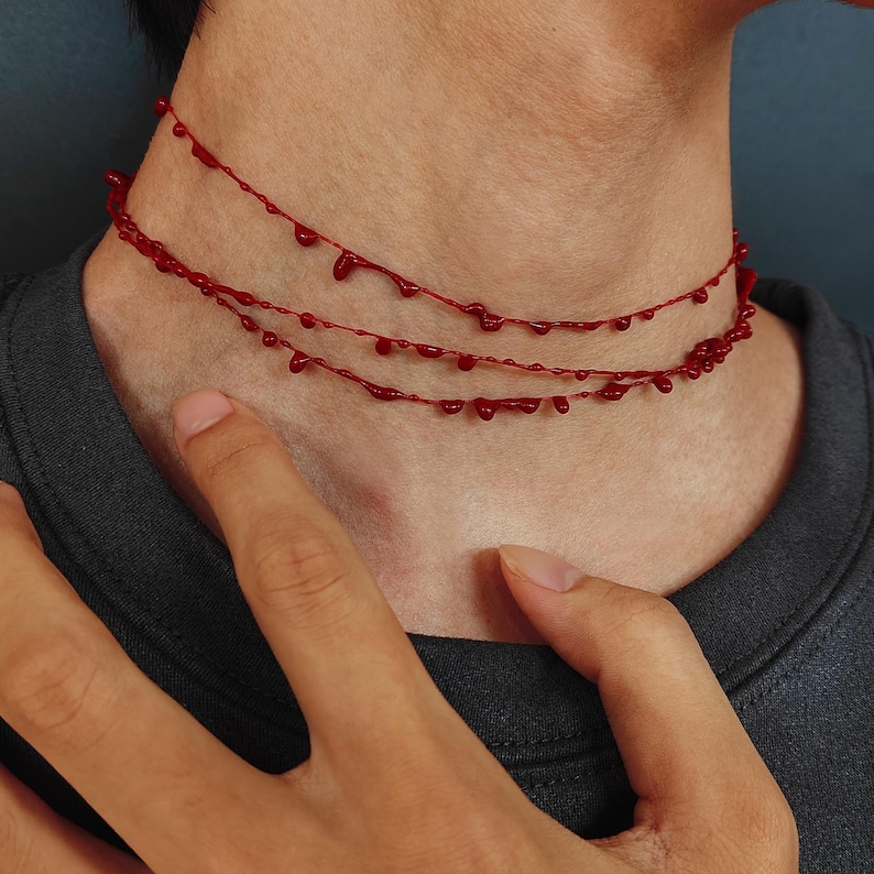 Puede incluir: Un collar rojo con tres hilos, cada uno adornado con cuentas en forma de gotas. El collar se lleva alrededor del cuello, creando un accesorio &uacute;nico y llamativo. Las cuentas est&aacute;n espaciadas uniformemente.
