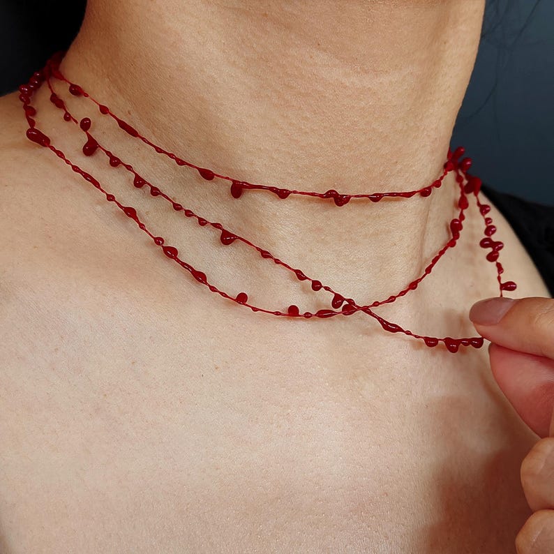 Puede incluir: Un collar rojo de tres hilos con un dise&ntilde;o de goteo. El collar est&aacute; hecho de finos cordones rojos con cuentas en forma de l&aacute;grima espaciadas uniformemente. El collar se lleva alrededor del cuello.