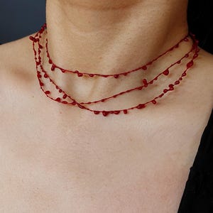 Puede incluir: Un collar rojo de tres hilos con un dise&ntilde;o &uacute;nico. Cada hilo presenta peque&ntilde;os elementos en forma de l&aacute;grima, espaciados uniformemente. El collar se lleva alrededor del cuello, mostrando su estilo art&iacute;stico distintivo. Un accesorio audaz y llamativo.
