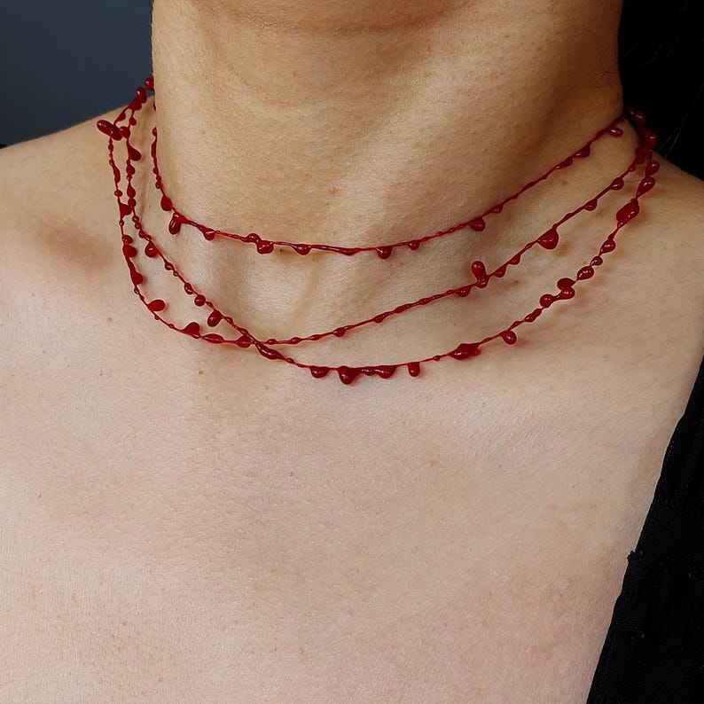 Puede incluir: Un collar rojo de tres hilos con un dise&ntilde;o &uacute;nico. Cada hilo presenta peque&ntilde;os elementos en forma de l&aacute;grima, espaciados uniformemente. El collar se lleva alrededor del cuello, mostrando su estilo art&iacute;stico distintivo. Un accesorio audaz y llamativo.
