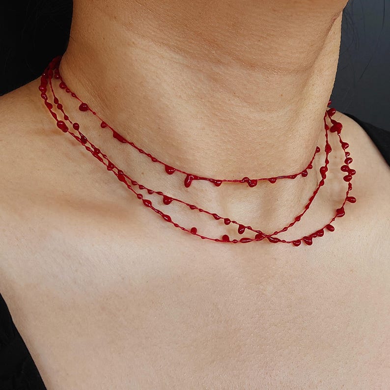 Puede incluir: Un collar rojo de tres hilos con un dise&ntilde;o &uacute;nico. Cada hilo presenta peque&ntilde;as cuentas en forma de gota, creando un accesorio delicado y llamativo. El collar se lleva alrededor del cuello, mostrando su color vibrante y su estilo distintivo.