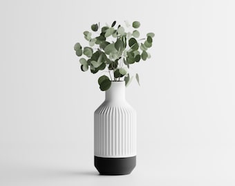 May include: A white ceramic vase with vertical ribbed detailing and a black base, holding a collection of green eucalyptus leaves. The vase has a modern, minimalist design, perfect for home decor.