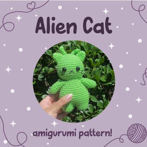 Puede incluir: Un amigurumi de Alien Cat verde tejido a ganchillo con ojos negros y boca cosida. El texto "Alien Cat" está encima del gato y "amigurumi pattern!" debajo. El fondo es un círculo de follaje verde sobre un fondo lavanda.