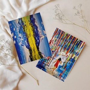 Peut inclure: Deux impressions d'art sur une surface blanche. L'une présente un paysage abstrait avec des couleurs bleues, jaunes et blanches. L'autre représente une personne en robe rouge avec un parapluie blanc sous une pluie colorée.
