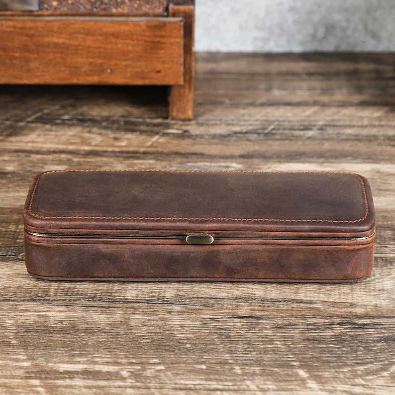 Peut inclure: Une bo&icirc;te rectangulaire en cuir marron avec un couvercle &agrave; charni&egrave;re et un fermoir en m&eacute;tal. La bo&icirc;te est en cuir vieilli et pr&eacute;sente des coutures visibles sur les bords. La bo&icirc;te mesure environ 20 cm de long.