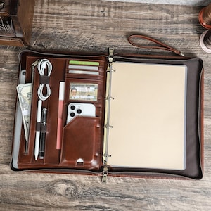 Peut inclure: Un porte-documents zippé en cuir marron doté d'un mécanisme à trois anneaux, de plusieurs fentes pour cartes, d'une fenêtre transparente pour pièce d'identité, d'une poche pour smartphone, d'un porte-stylo et d'un compartiment zippé.