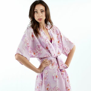 May include: A woman wearing a light purple floral print robe with a short sleeve and a tie belt.