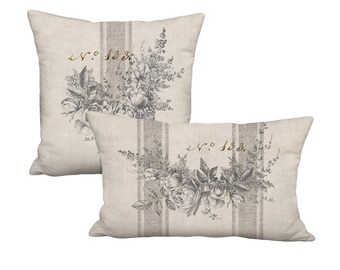 May include: Two decorative throw pillows with a beige linen fabric background. The pillows feature a black and white floral design with a gold script that reads "No. 183."