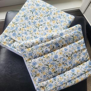 May include: Two floral print pouches with a white zip and a silver ring pull. The pouches feature a pattern of blue and yellow flowers on a white background. The top pouch is rectangular, and the bottom pouch is quilted.