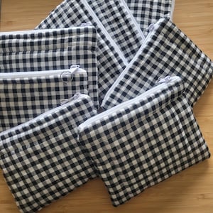 May include: Several black and white gingham zippered pouches of different sizes. Each pouch features a white zip. The pouches are arranged on a wooden surface. The fabric has a classic checkered pattern.