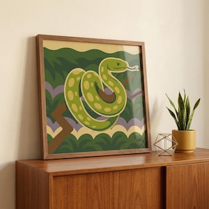 May include: A framed art print depicting a green snake with yellow spots, set against a backdrop of green foliage and a light yellow sky. The artwork is in a wooden frame, displayed on a wooden cabinet.