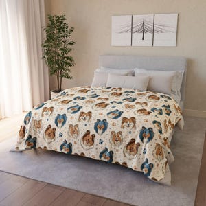 Puede incluir: Una manta color crema con un patrón repetido de caras de perros Sheltie en tonos marrones y azules. La manta también incluye huellas de patas y formas de estrellas. La manta está sobre una cama con almohadas blancas y un cabecero gris.