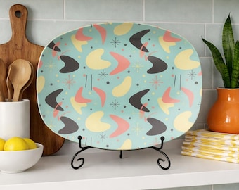 May include: A rectangular serving platter with a retro design. The platter features a light blue background with a pattern of gray, yellow, and pink boomerang shapes and starbursts. It is displayed on a black metal stand.