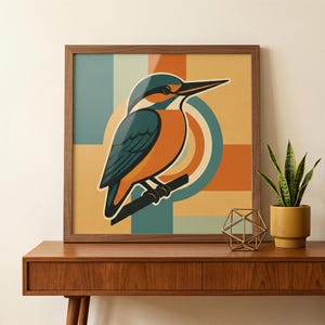 Puede incluir: Una impresión artística enmarcada con una ilustración estilizada de un martín pescador posado en una rama. El ave se representa en tonos naranja, verde azulado y negro sobre un fondo geométrico de verde azulado, naranja y amarillo. La obra está sobre una mesa de madera.