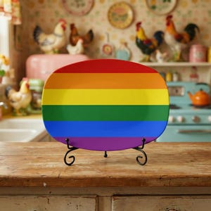 May include: A rectangular plate with a rainbow design, displayed on a black metal stand. The plate features horizontal stripes in red, orange, yellow, green, blue, and purple. The plate is set on a wooden surface.