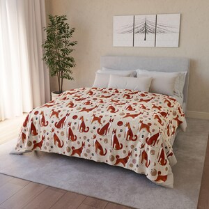 May include: A beige blanket with a repeating pattern of brown dogs, paw prints, and circular shapes. The blanket is spread over a bed with white pillows and a gray headboard. The room has a neutral color scheme.