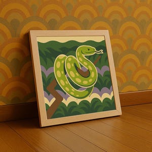 May include: A framed art print depicting a green snake with yellow spots, coiled around a brown branch. The background features green foliage, purple accents, and a yellow sky. The frame is made of light-coloured wood.