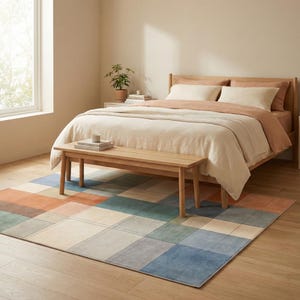 May include: A bedroom scene featuring a wooden bed frame with beige bedding and a matching bench at the foot of the bed. A colorful geometric rug in shades of blue, orange, and green covers the floor. A small potted plant sits on a nightstand.