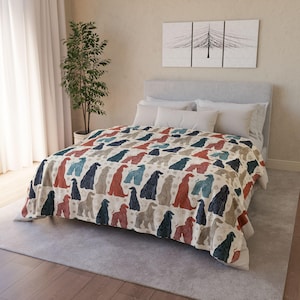 May include: A beige blanket with a repeating pattern of stylized dog silhouettes in shades of red, blue, and gray. The blanket is spread over a bed with white pillows and a gray headboard. A decorative tree painting hangs above the bed.