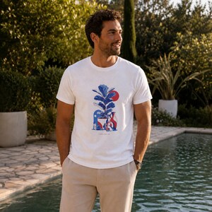 Peut inclure: Un t-shirt blanc à manches courtes avec un imprimé graphique central représentant un figuier lyre en pot, un soleil rouge et des vases en céramique bleus et rouges. Le t-shirt possède un col rond et est porté avec un pantalon beige clair.