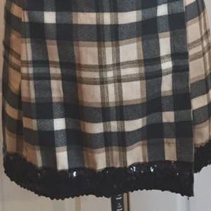 May include: A plaid skirt in black, tan, and white, with a black sequined hem. The skirt is displayed on a mannequin. The plaid pattern features intersecting lines of varying widths, creating a classic design.