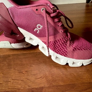May include: Close-up of a pair of athletic shoes in a deep magenta color. The shoes have white soles and laces, with the brand logo visible on the side. The mesh upper provides breathability, and the design suggests a focus on comfort and performance.