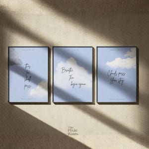 Pode incluir: Três impressões de arte emolduradas com um céu azul claro e um design de nuvens. Cada impressão apresenta uma citação inspiradora diferente em escrita elegante: "This too shall pass", "Breathe Then Begin again" e "Clouds pass You stay."