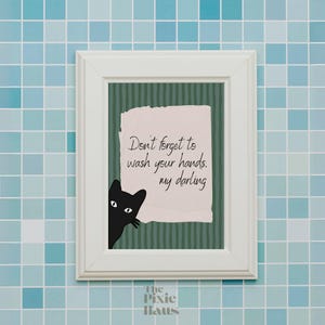 Pode incluir: Arte de parede emoldurada em branco com fundo listrado verde e branco. A arte apresenta um papel rasgado com o texto "Não se esqueça de lavar as mãos, meu querido". Um gato preto espreita do lado esquerdo.