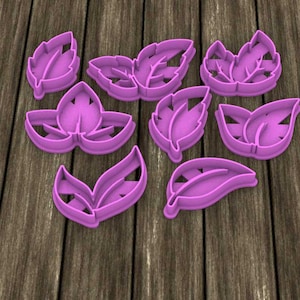 Puede incluir: Colección de ocho cortadores de galletas morados con forma de hoja. Los cortadores varían en tamaño y diseño, algunos con detalles intrincados de venas. Están dispuestos sobre una superficie de madera, ideales para hornear o manualidades.