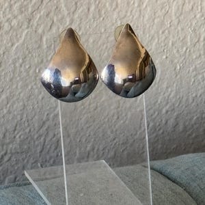 May include: A pair of silver teardrop-shaped earrings. The earrings are smooth and shiny.