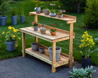 May include: A wooden potting bench with two shelves, holding various potted plants and a decorative vase. The bench is made of light-colored wood and is set outdoors on a stone surface, surrounded by greenery.