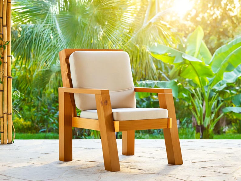 May include: A wooden outdoor armchair with a light beige cushion and backrest. The chair has a natural wood finish and is set on a stone patio. The background features lush green foliage and sunlight.