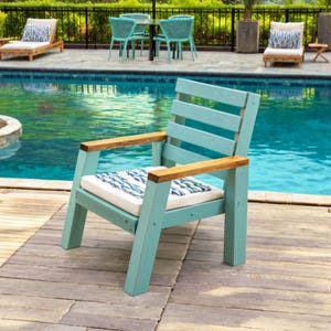 May include: A light blue outdoor armchair with wooden armrests and a white cushion with a blue and white pattern. The chair is made of wood and is placed on a wooden deck next to a pool.